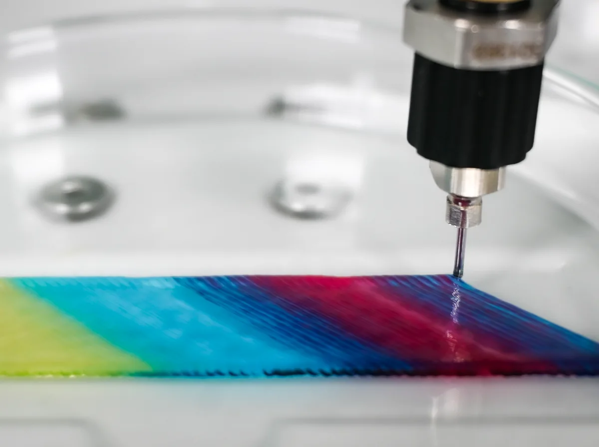 Bioprinting nozzle depositing a multicolored material gradient