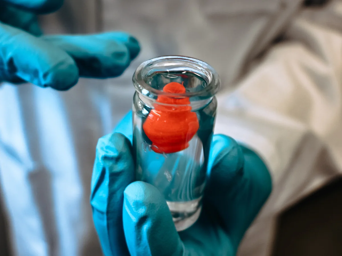 Gloved hands holding a vial containing a red tissue model